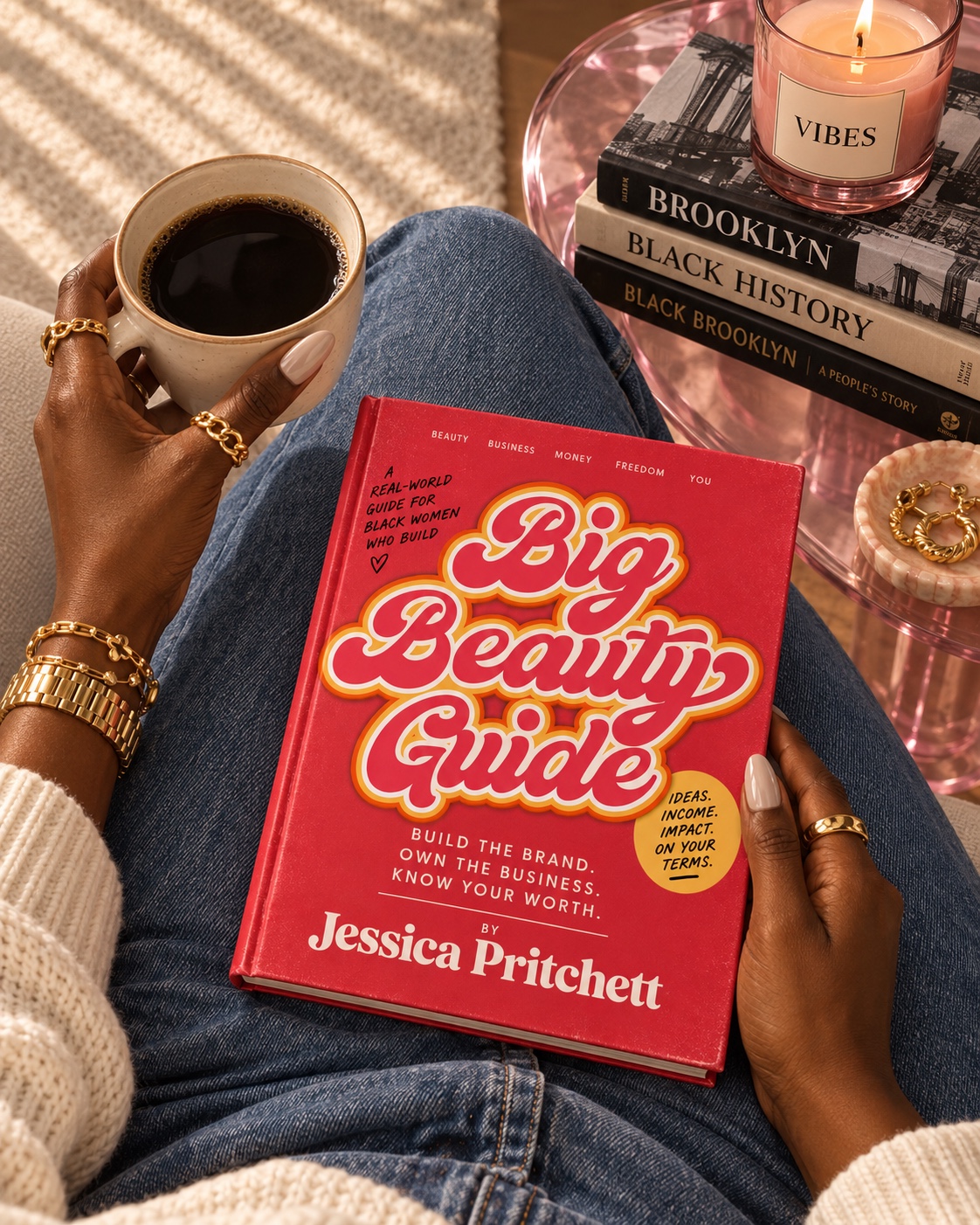 A woman holding The Big Beauty Guide, with coffee, gold jewelry, and a pink candle